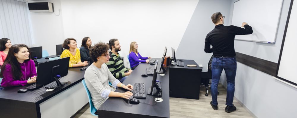 Formador explica un tema frente a una pizarra mientras los alumnos siguen la clase.