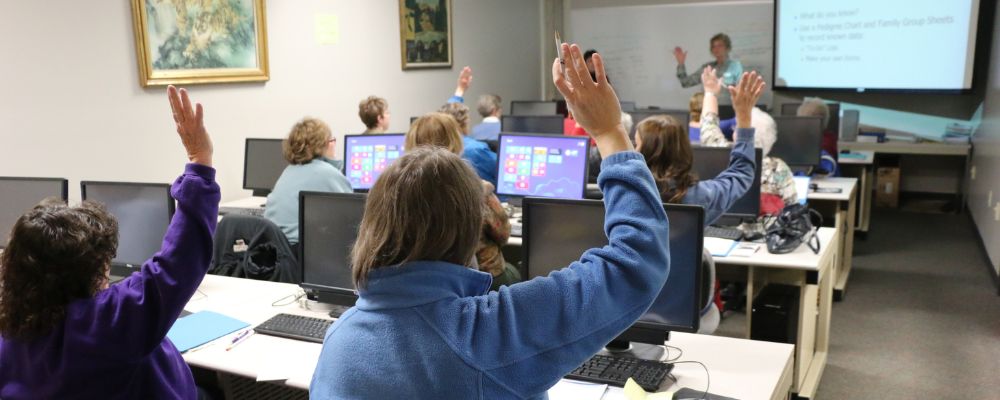 Alumnos participan en una clase de informática levantando la mano.